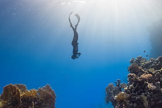 A scuba diver diving to the bottom of the ocean alone