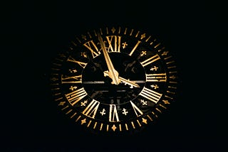 A large clock face in night, gold numbers and hands, black clock face.