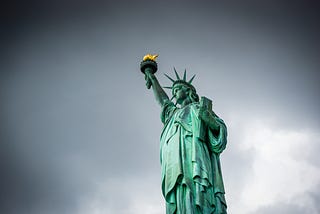 Photo of the Statue of Liberty by Jason Krieger, via Unsplash, against a grey backdrop