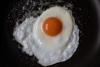 A cracked egg frying on a pan.