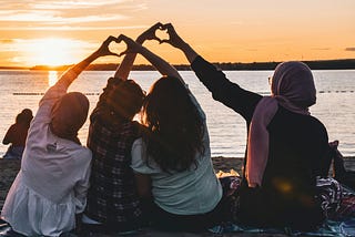 A group of friends sitting by the water embracing them arms and hands with the heart symbol