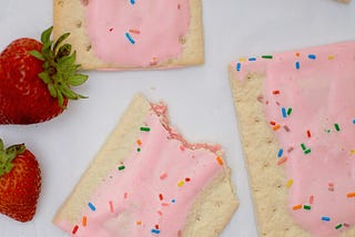 Homemade strawberry pop-tart pastries with sprinkles alongside two strawberries