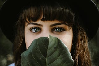 A woman looks out from behind a large leaf.