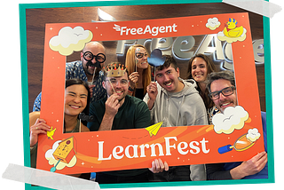 Seven members of the FreeAgent Design team, including Finn McEwan, the author of this piece, pose within a large illustrated picture frame created for FreeAgent’s LearnFest.