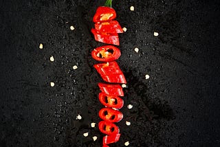 picture shows the chilli is cut into various parts and displayed on the black surface and sprinkled with water