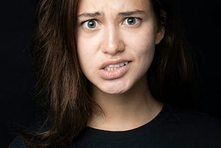 A 20-something year old Caucasian girl with brown hair, wearing a black shirt and staring straight ahead with a confused look on her face.