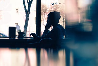 Silhouette of a man sitting at a table looking at a laptop