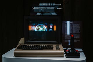 A dark room with a Commodore 64 keyboard, a small colour monitor, and a joystick.