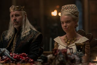 Viserys and Rhaenyra sitting together at the top table at a feast which is set to start the beginning of the Royal Wedding festivities.