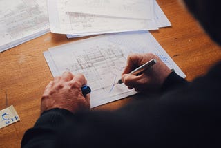 A man at a desk drawing on architectural blueprints