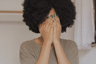 Black woman covering her face with her hands.