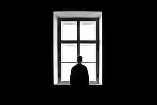 Lonely person in dark room looking through window