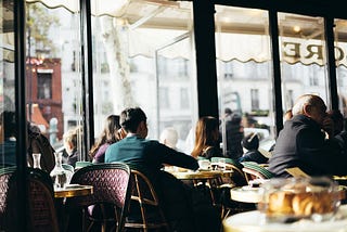 Inside the Café de Flore, customers enjoying drinks and pastries, with a view out the cafe window.