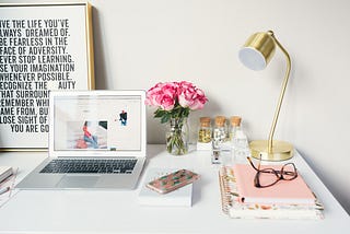 An organize desk with a laptop, lamp, flower, eyeglasses, a motivational standing board.