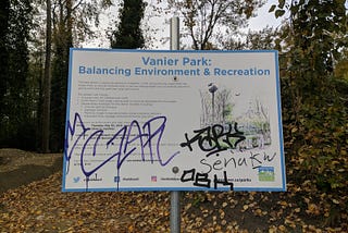An informational poster in Vanier Park with multiple acts of graffiti, including “Senakw”, scrawled in permanent marker.