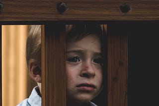 A child with a sad face staring desperately through the bars of a railing.