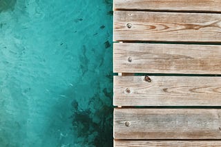 An abstract image divided horizontally, with teal water on the left and light brown deck boards on the right.