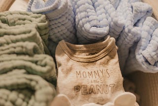 An image of a wicker basket with soft baby blankets in blues and greens, neatly folded next to folded baby clothes.