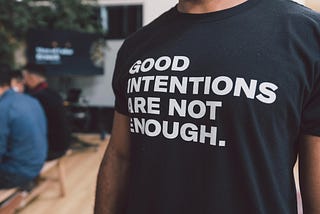 This is a photo of a person wearing a tshirt that says “good intentions are not enough”