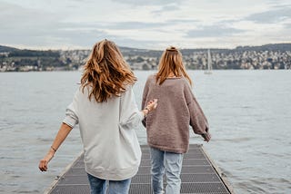 back of two girls in sweaters walking towards end of dock