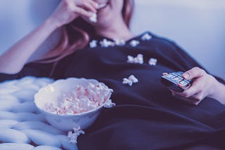 A woman eating popcorn while watching a movie from home. These are the best holiday movies to watch.