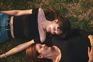 A mother and daughter lying on the ground and smiling at each other.
