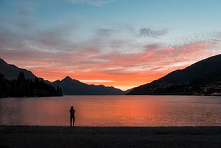 A person watching the sun set over water and mountains