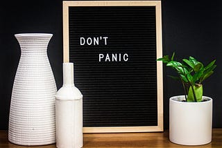 A still life featuring three vases, one containing a plant. There is also a blackboard with the words, Don’t Panic.