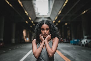 A woman with a straight face standing in the middle of an empty road.