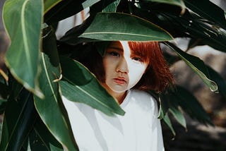 A woman shielding her face from the bright sunlight with some leaves.