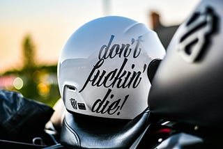 A picture of a white motorcycle helmet with black words that read, “don’t fucking die!” to pass across the message to keep going