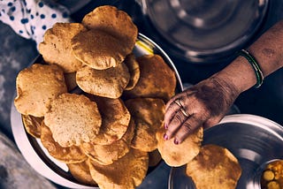 A woman’s hand that is picking up puris served on a plate.