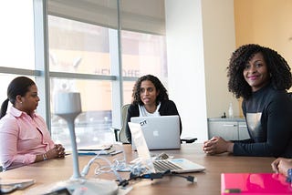 Three women of color sitting at a table with computers.