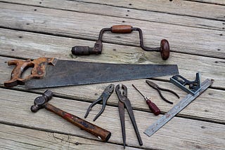 Old tools, their handles brown with age, are arrayed on a weathered wooden floor.