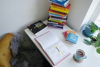 a desk with a stack of books about design topics, and an open book with a cup of tea next to it