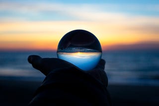 A hand holding a crystal sphere in which a sunset is reflected, and which is inverted in this sphere.