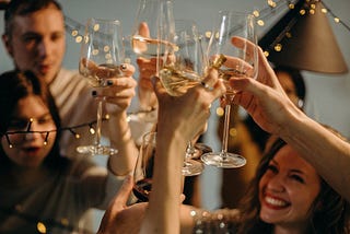 Six people gather around to raise their glasses for a celebration. There are fairy lights and the mood is happy, warm, and fuzzy.