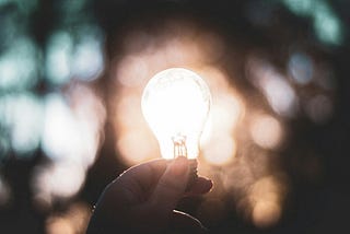 A photograph of a hand holding an illuminated light bulb