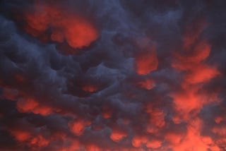 A brooding sky of dark clouds and sun burning through a deep orange