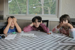 Three kids at a kitchen table making see, hear, and taste gestures.