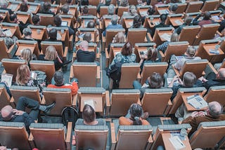A high-angle image of a group of people sitting in rows of chairs, like an auditorium