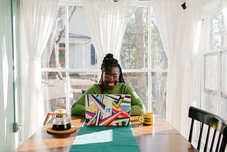 Woman sitting at dining table in front of laptop, smiling.