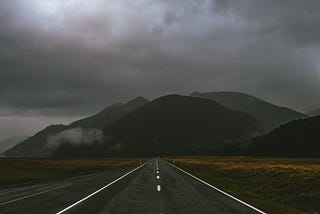 A photo of a dark highway leading toward dark mountains.