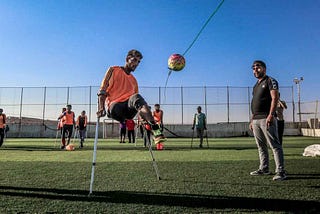 A man a crutches, feet in the air, kicking a ball in a sports game