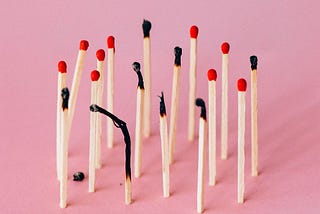 Eighteen matches standing upright, some unlit and others burned out, against a pink background.