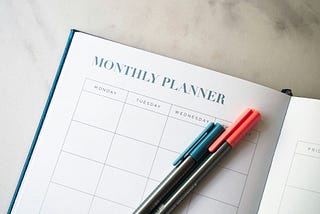 A monthly planner with a blue and pink marker laying on top.