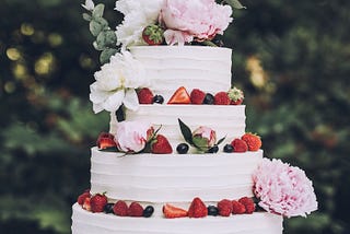 Layer cake with white frosting, fresh fruit, and fresh flowers