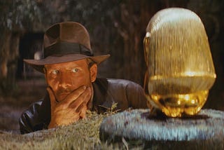 Harrison Ford as Indiana Jones pondering the weight of a golden artifact he is about to pilfer.