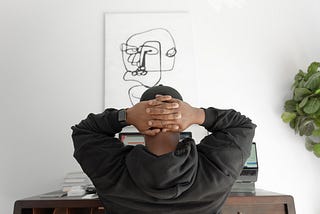 Stressed man sitting at his desk staring at his computer with hands clasped behind his head.