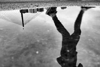 The reflection of a jogger in a puddle, the photo is black and white.